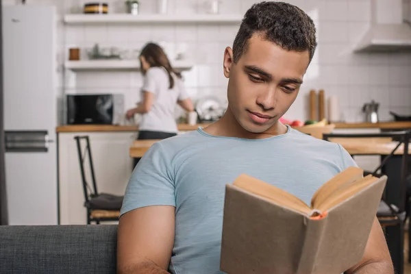 Selective focus of handsome mixed race man reading book at home — Stock Photo