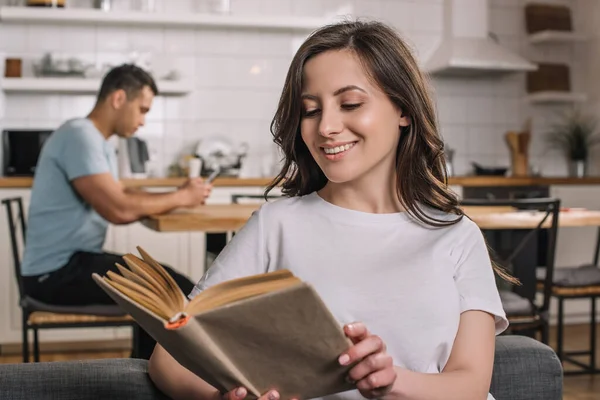 Selective focus of cheerful woman reading book near mixed race man at home — Stock Photo