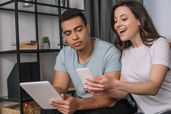 Enfoque selectivo de pareja interracial utilizando gadgets en la sala de estar - foto de stock