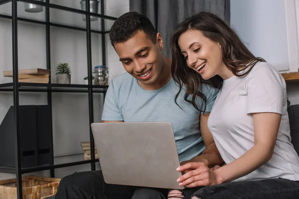 Cheerful girl and mixed race freelancer using laptop — Stock Photo