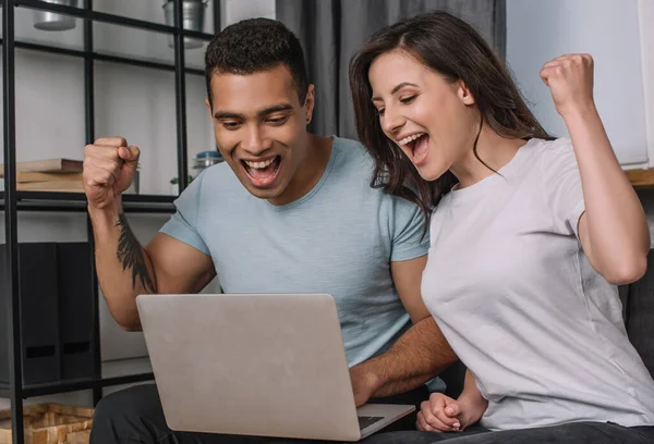 Cheerful interracial couple celebrating while looking at laptop — Stock Photo