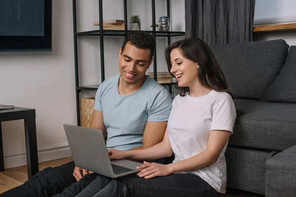 Alegre interracial casal usando laptop em casa — Fotografia de Stock