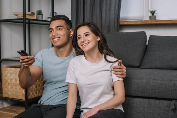 Feliz mixto raza hombre celebración mando a distancia cerca alegre novia - foto de stock