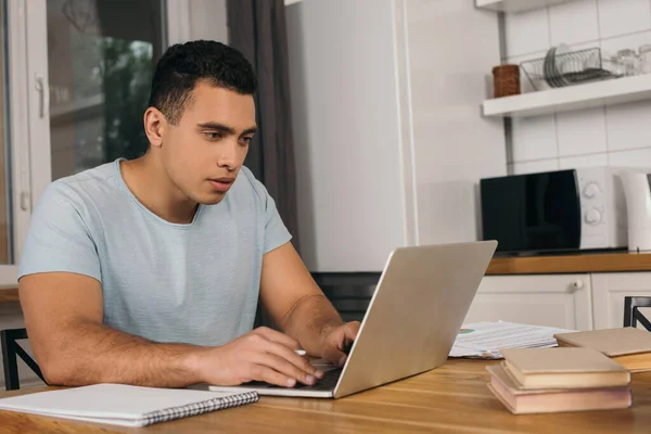 Beau freelance mixte utilisant ordinateur portable près de livres et ordinateur portable — Photo de stock