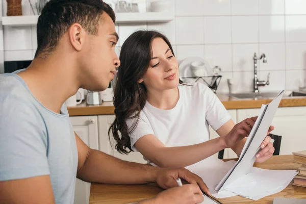 Selective focus of woman holding papers near mixed race boyfriend at home — Stock Photo