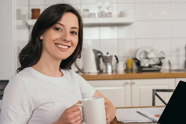 Cheerful woman holding cup and looking at camera — Stock Photo