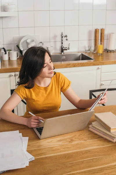 Freelancer feliz usando el ordenador portátil y mirando los papeles cerca de los libros en la mesa - foto de stock