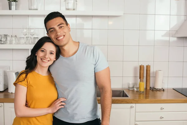 Gai mixte race homme étreignant heureux copine dans la cuisine — Photo de stock