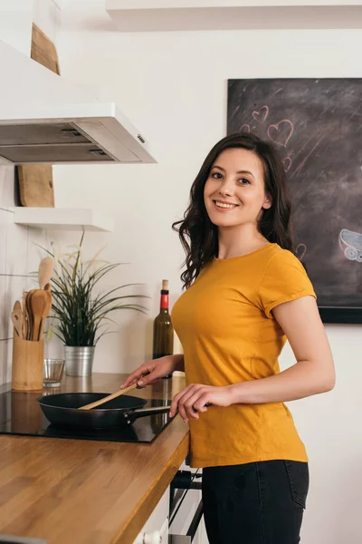 Весела жінка тримає дерев'яний шпатель біля сковороди — стокове фото