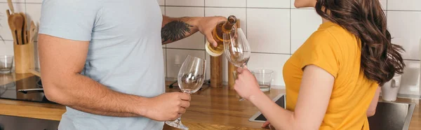 Panoramic concept of mixed race man holding bottle of wine near glasses and girlfriend — Stock Photo