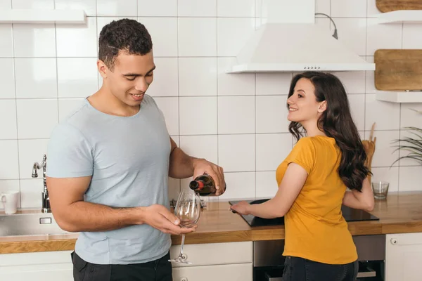 Mixed race man holding bottle of wine near glass and cheerful girlfriend — Stock Photo
