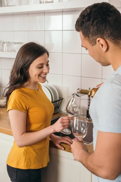 Selektiver Fokus des gemischten Rassenmannes mit Weinflasche in der Nähe von Gläsern und lächelnder Freundin — Stockfoto