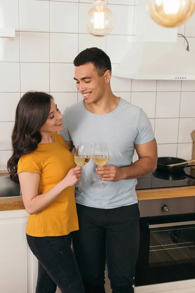 Selective focus of happy interracial couple clinking glasses of white wine at home — Stock Photo