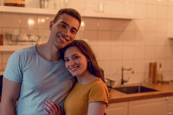 Glückliches multiethnisches Paar lächelt, während es sich zu Hause umarmt — Stockfoto