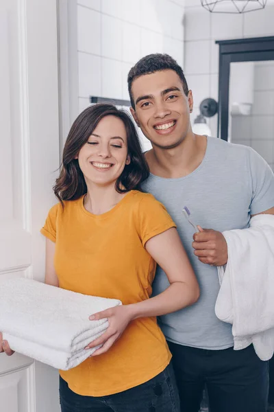 Feliz pareja multirracial sosteniendo toallas en el baño - foto de stock