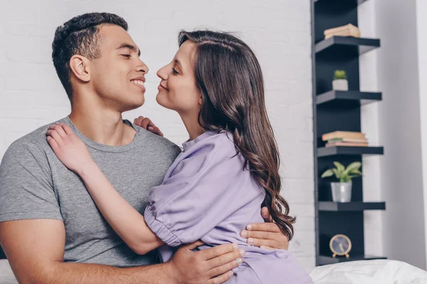 Hombre de raza mixta y mujer alegre abrazándose en casa - foto de stock