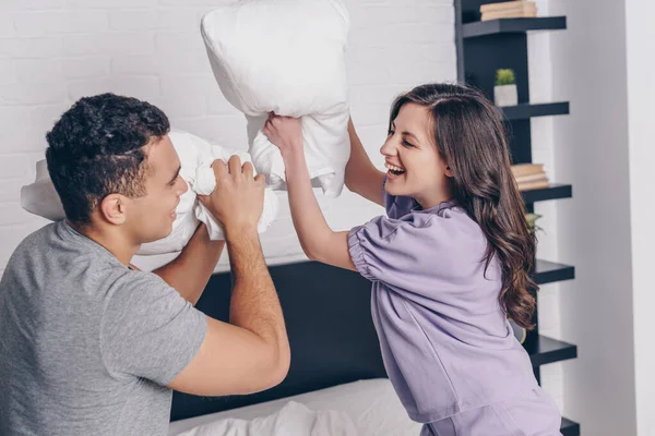 Cheerful interracial couple pillow fighting in bedroom — Stock Photo