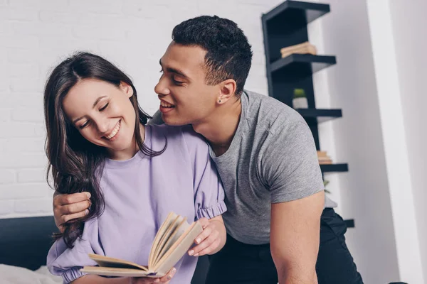 Beau mixte homme de race regardant sourire fille livre de lecture — Photo de stock