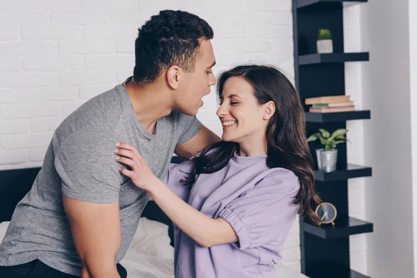Bi-racial hombre abrazando alegre chica en el dormitorio - foto de stock