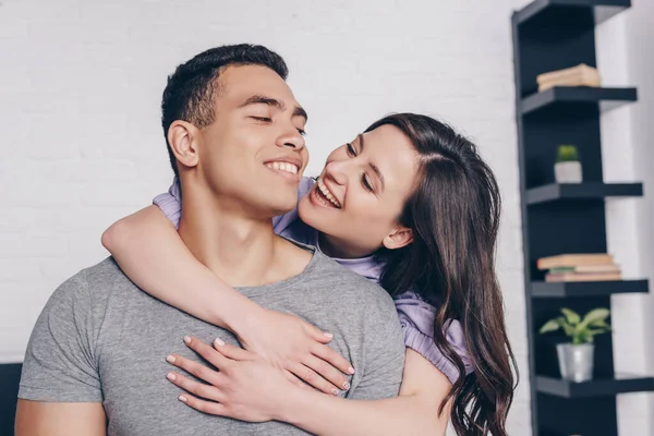 Cheerful woman embracing handsome bi-racial man in bedroom — Stock Photo