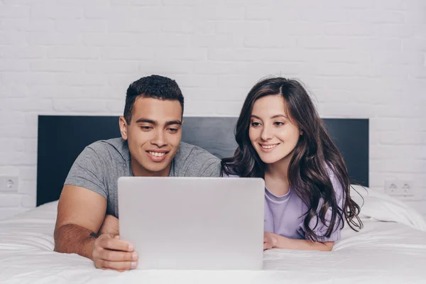 Bi-racial homem e atraente mulher rede ao usar laptop no quarto — Fotografia de Stock