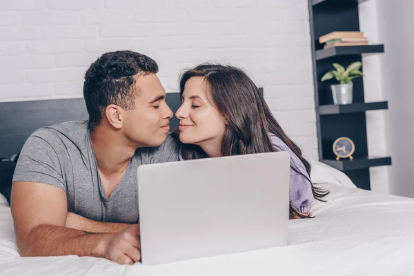 Uomo bi-razziale e donna attraente con gli occhi chiusi vicino al computer portatile sul letto — Foto stock