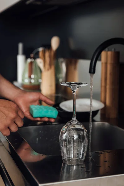 Selective focus of wet glass near man holding sponge in kitchen — Stock Photo