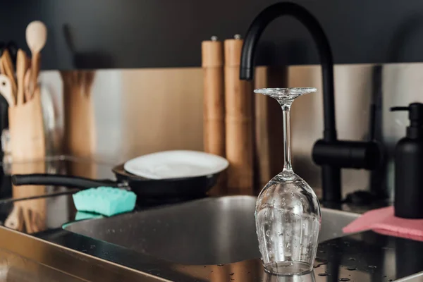 Selective focus of wet glass on surface near sink and faucet in kitchen — Stock Photo