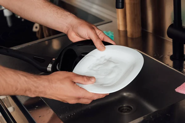 Cropped view of man holding wet plate and frying pan near sink in kitchen — Stock Photo