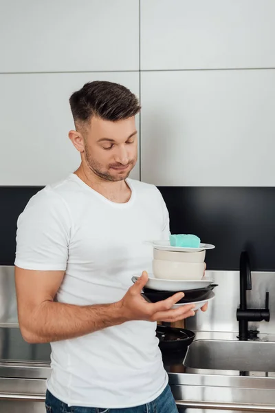 Недовольный человек держит грязные тарелки на кухне — стоковое фото