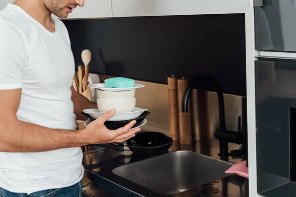 Cropped view of man holding dirty plates and sponge in kitchen — Stock Photo