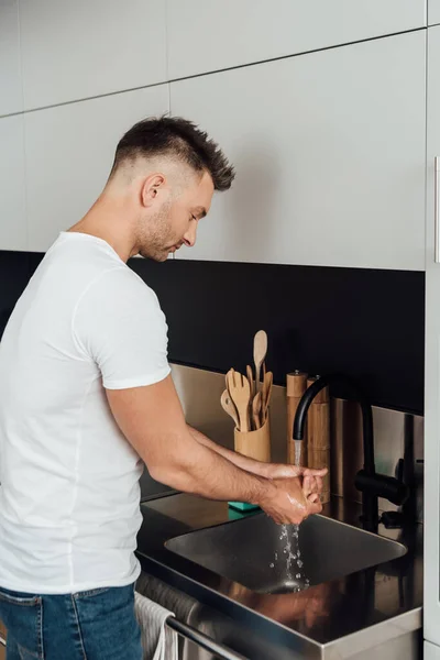 Homem bonito lavar as mãos perto de pia na cozinha — Fotografia de Stock