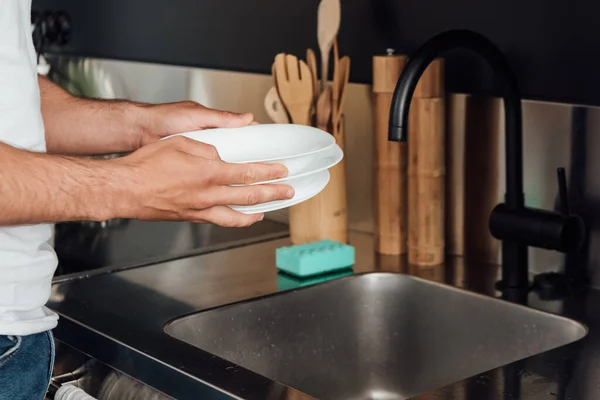 Vista recortada del hombre sosteniendo platos blancos en la cocina - foto de stock