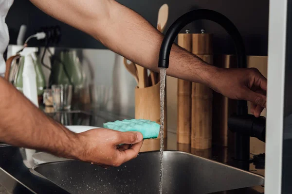 Vue recadrée de l'homme tenant éponge près de l'eau du robinet — Photo de stock