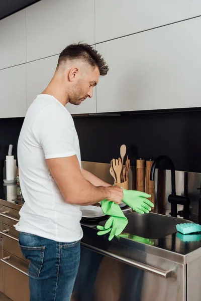 Homem bonito usando luva de borracha na cozinha — Fotografia de Stock