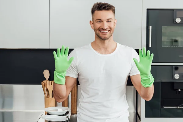 Hombre alegre mostrando las manos en guantes de goma en casa - foto de stock