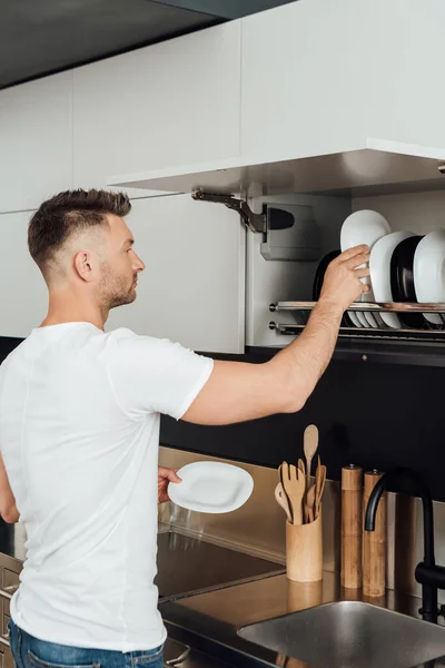 Handsome man putting clean plates in plate dryer — Stock Photo