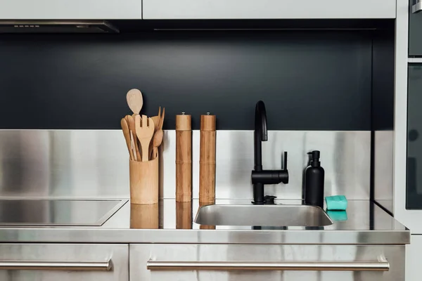 Wooden pepper mill and salt mill near faucet, sink, soap dispenser and sponge in kitchen — Stock Photo