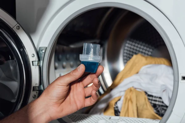 Cropped view of man holding measuring cup with detergent near washing machine with dirty clothing — Stock Photo