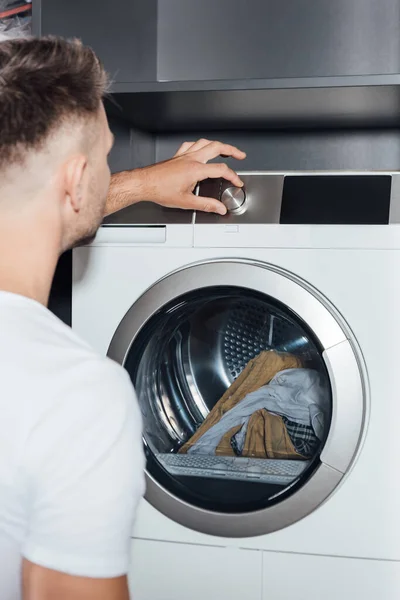 Foco seletivo do homem tocando botão na máquina de lavar roupa moderna com lavanderia suja — Fotografia de Stock
