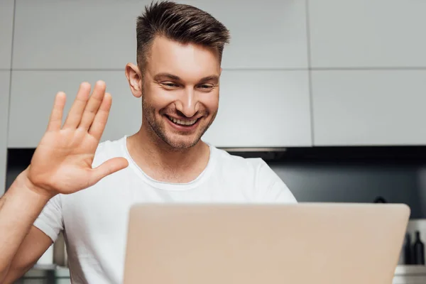 Selektiver Fokus eines glücklichen Mannes, der mit der Hand winkt und Videotelefonie hat — Stockfoto