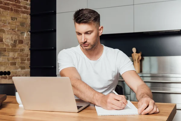 Homme concentré tenant stylo et regardant ordinateur portable tout en étude en ligne — Photo de stock