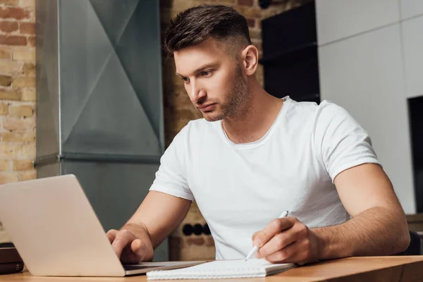 Сфокусированный человек держит ручку и смотрит на ноутбук во время онлайн-исследования — стоковое фото