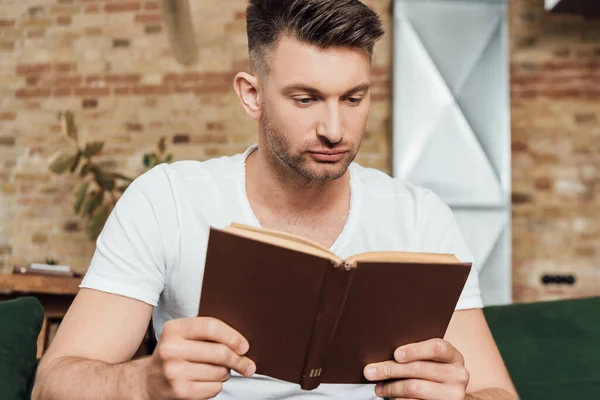 Selektiver Fokus des gutaussehenden Mannes, der zu Hause Buch liest — Stockfoto