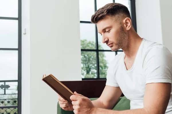 Hombre leyendo libro mientras está sentado en el sofá en la sala de estar - foto de stock