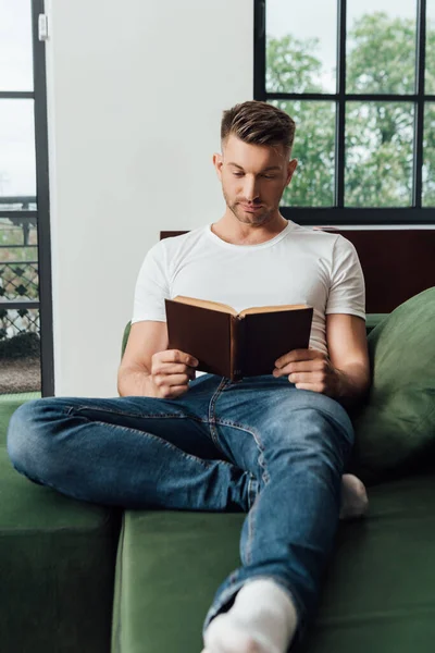 Foco seletivo do homem ler livro no sofá em casa — Fotografia de Stock