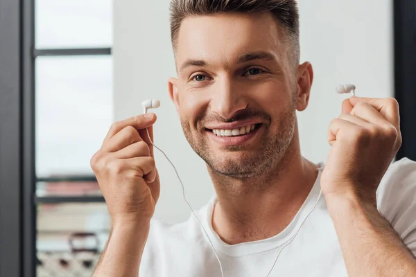 Beau homme souriant tenant des écouteurs à la maison — Photo de stock