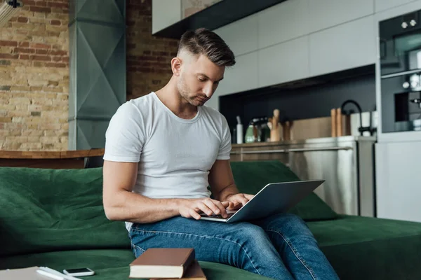 Вибірковий фокус працівника з використанням ноутбука біля книг і паперів на дивані — стокове фото