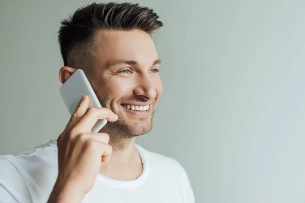 Красивий чоловік посміхається, розмовляючи на смартфоні ізольовано на сірому — стокове фото