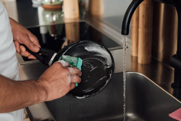 Vista recortada de la sartén de limpieza hombre en la cocina - foto de stock